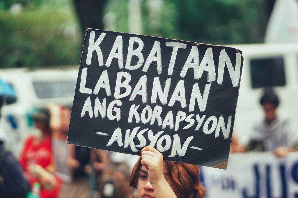A protester holds a sign against corruption in a urban street setting.