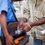 A man exchanges needles on a street in Dhaka, Bangladesh, highlighting public health efforts.