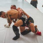Two male athletes engage in intense grappling during MMA training session indoors.