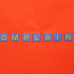 Blue letter tiles spelling 'COMPLAINT' on a vibrant red surface.