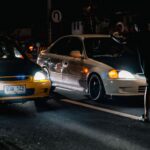Dramatic night shot capturing street car racing with onlookers and vivid headlights.