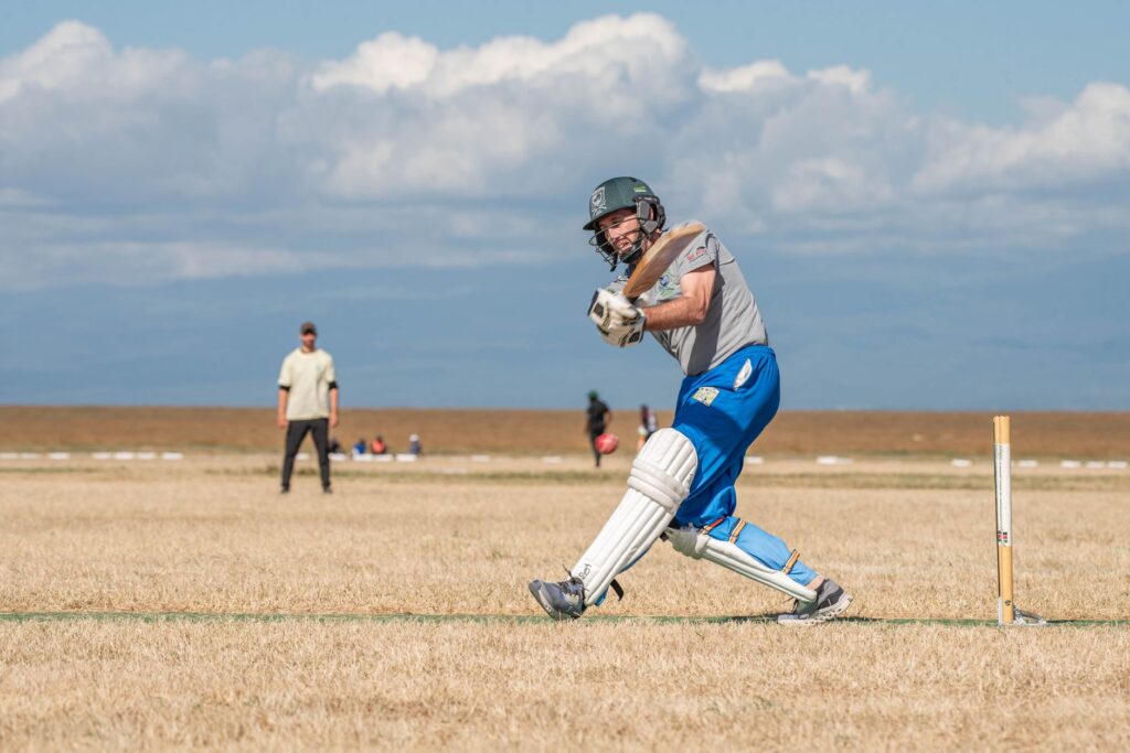 Cricketer hitting the ball during a match on a sunny day, showcasing athletic action and skill.