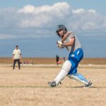 Cricketer hitting the ball during a match on a sunny day, showcasing athletic action and skill.