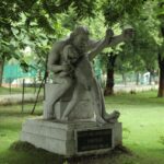 Sculpture of Eklavya and Dronacharya, Raipur, India, amidst lush greenery.