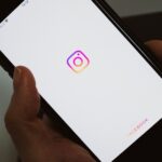 Crop faceless person taking mobile phone and demonstrating blank screen with social media app logo while having break and surfing internet