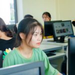Asian students focused on studying technology in a bright computer classroom setting.