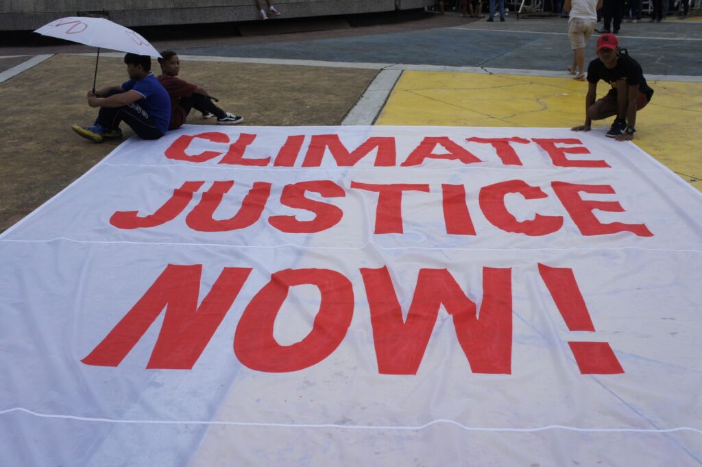 Large protest banner reading 'Climate Justice Now!' displayed outdoors during a demonstration.