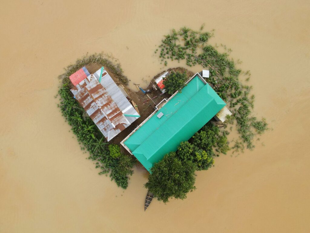 Top-down view of a flood-affected area in Bangladesh showing buildings and surrounding submerged land.