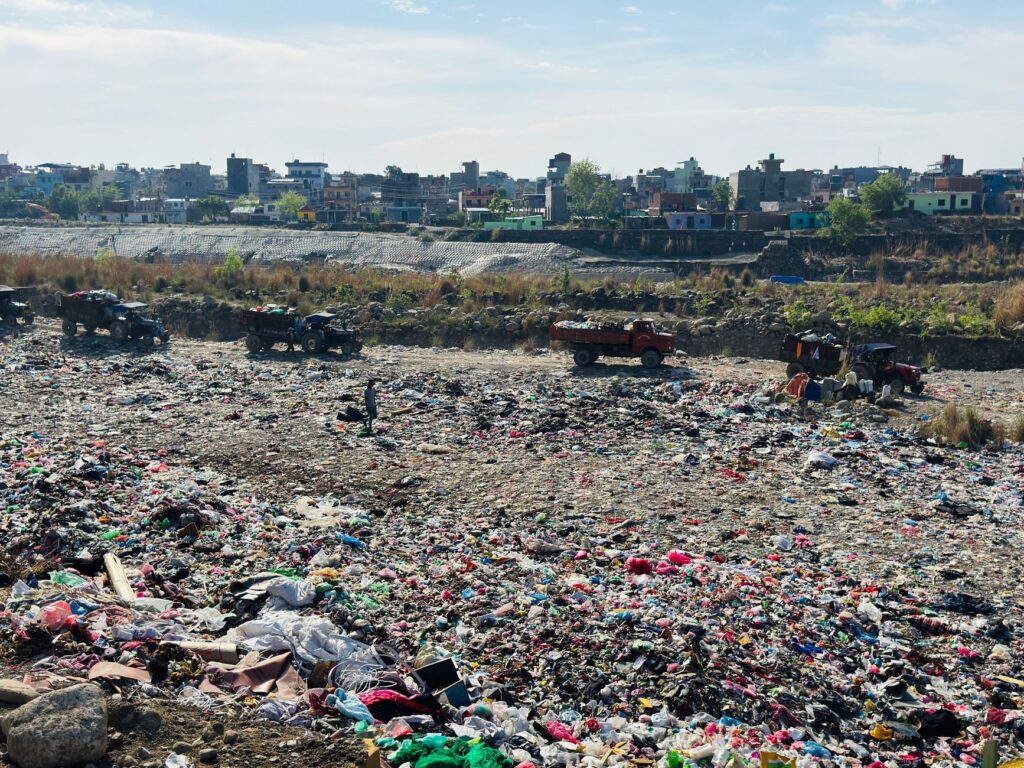 A landfill site in Butwal, Nepal with trucks amidst garbage disposal scene under clear sky.