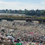 A landfill site in Butwal, Nepal with trucks amidst garbage disposal scene under clear sky.