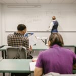 Students in a college classroom taking an exam with rules written on the board.