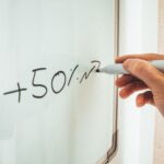 Crop anonymous male teacher writing math formulas on whiteboard during lessons in modern classroom