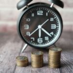 Stacked coins and a classic alarm clock symbolize the value of time and money.