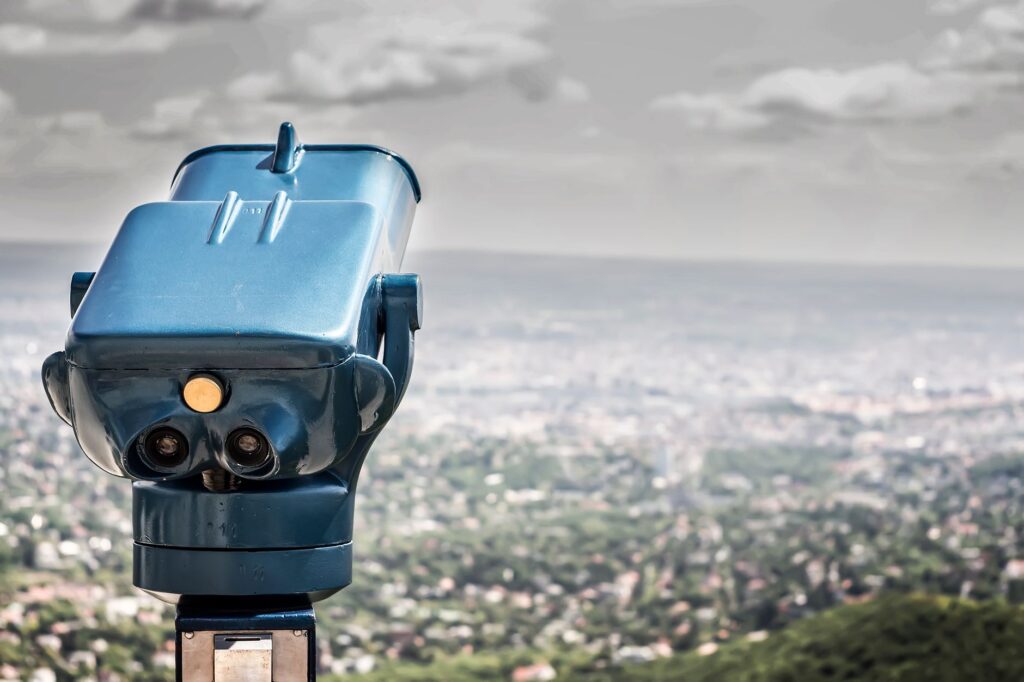 A coin-operated viewer overlooking a vast cityscape under a cloudy sky.