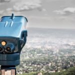 A coin-operated viewer overlooking a vast cityscape under a cloudy sky.