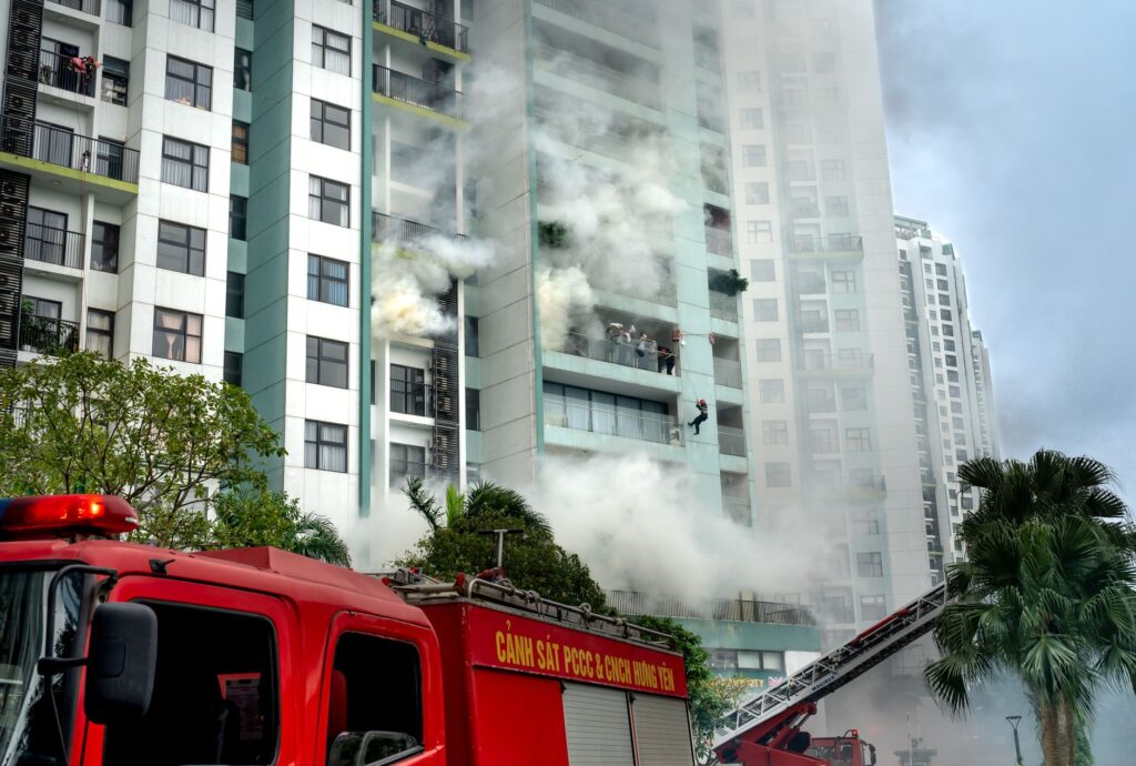 Firefighters respond to a building fire with smoke and emergency vehicles in an urban area.