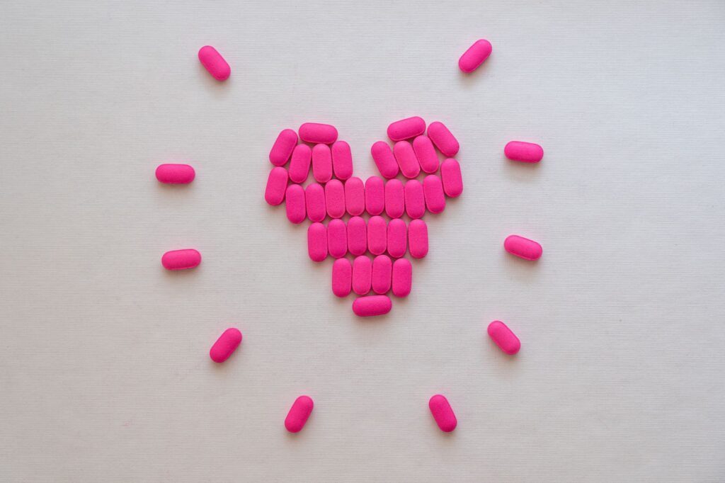 Pink pills arranged in a heart shape on a neutral surface. Perfect for health and medication themes.