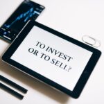 A tablet with text 'To Invest or To Sell?' on a white background.