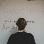 Person seen from behind writing Russian text on a wall in casual setting.