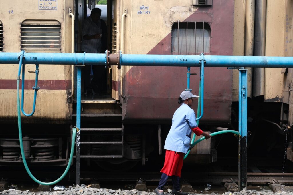 Woman in uniform refilling water into train at railway station. Public transportation service scene.