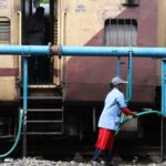 Woman in uniform refilling water into train at railway station. Public transportation service scene.