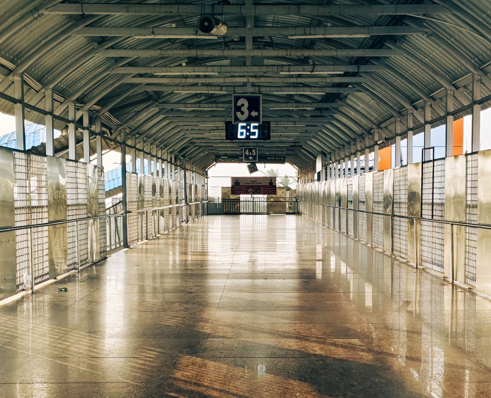 A deserted railway platform with a large digital clock, casting reflective patterns on the floor in Khordha, India.