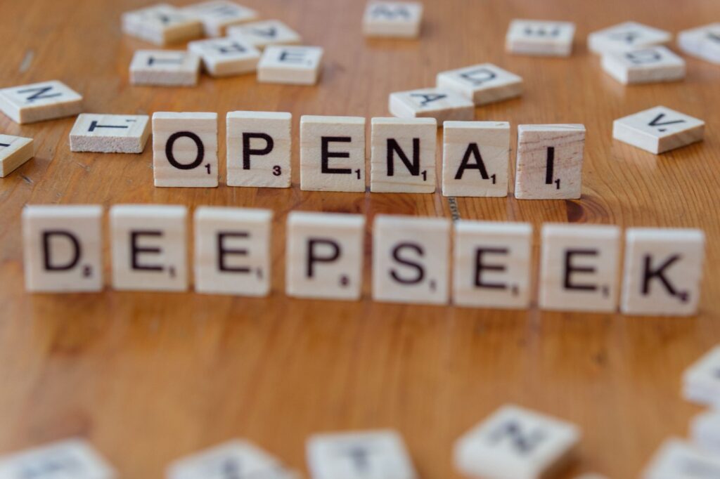 Close-up of wooden Scrabble tiles spelling OpenAI and DeepSeek on wooden table.