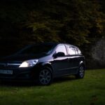 Black Opel Astra parked on grassy field in Skała, Poland during twilight.