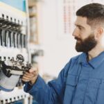 Bearded automobile mechanic selecting spray paint in a well-organized workshop with various tools.