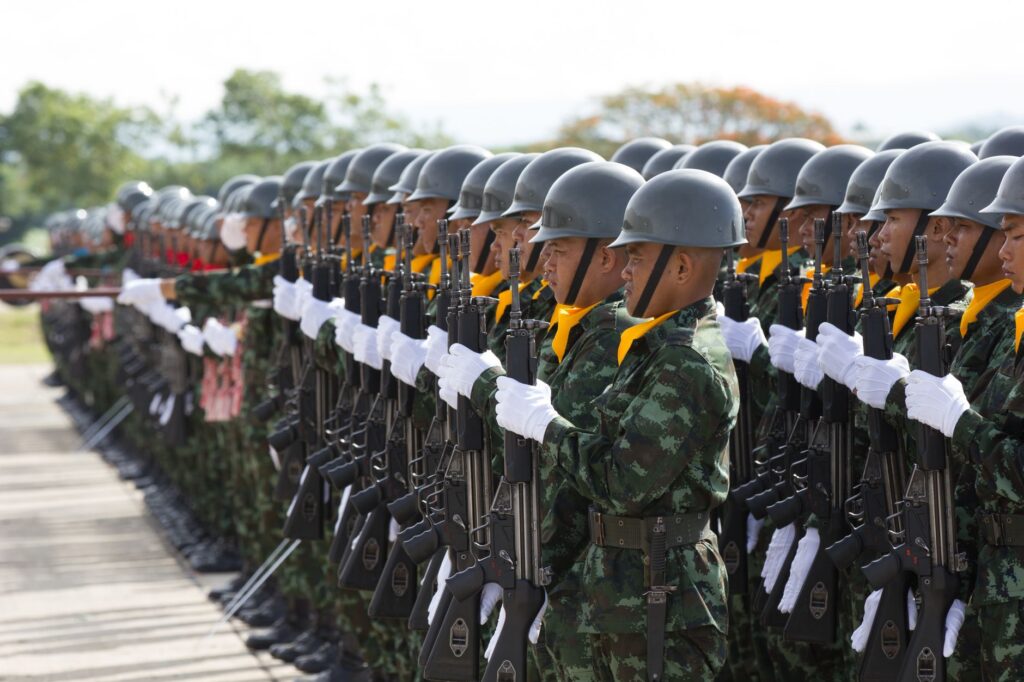 Side view Asian military troop in khaki uniform including white gloves and helmets marching with rifles in army