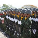 Side view Asian military troop in khaki uniform including white gloves and helmets marching with rifles in army