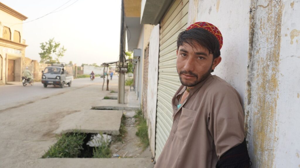 A young man wearing a traditional cap leaning against a wall on a city street, embracing local culture.