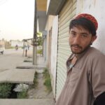 A young man wearing a traditional cap leaning against a wall on a city street, embracing local culture.
