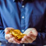 A person in a blue shirt holds a handful of shiny golden coins, symbolizing wealth and cryptocurrency.