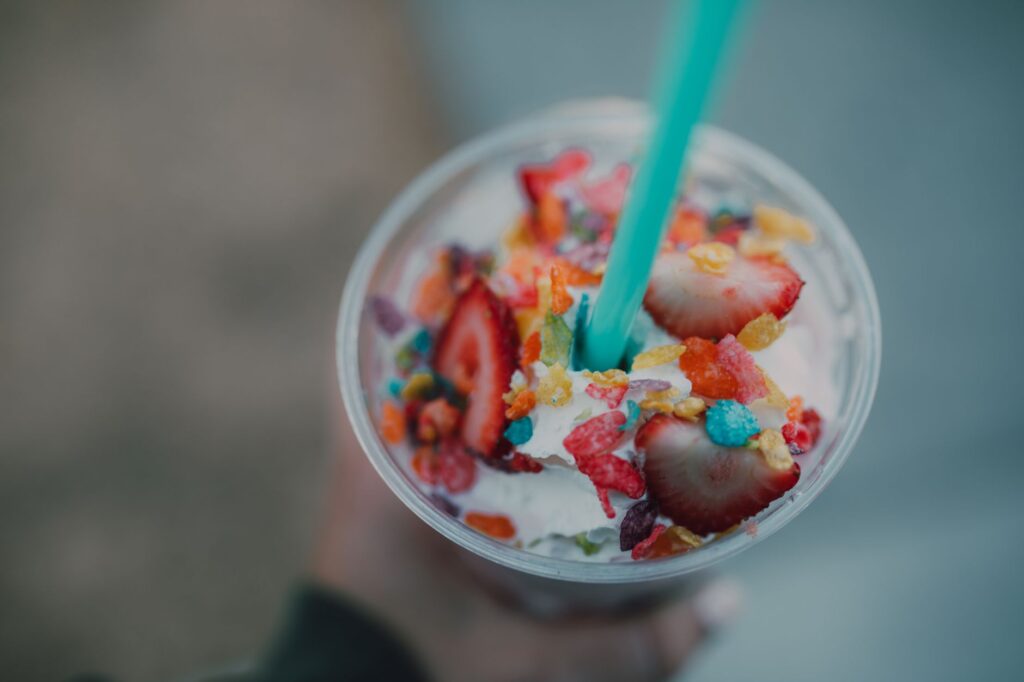 Close-up of a vibrant milkshake with strawberries and fruity cereal toppings.