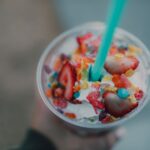 Close-up of a vibrant milkshake with strawberries and fruity cereal toppings.