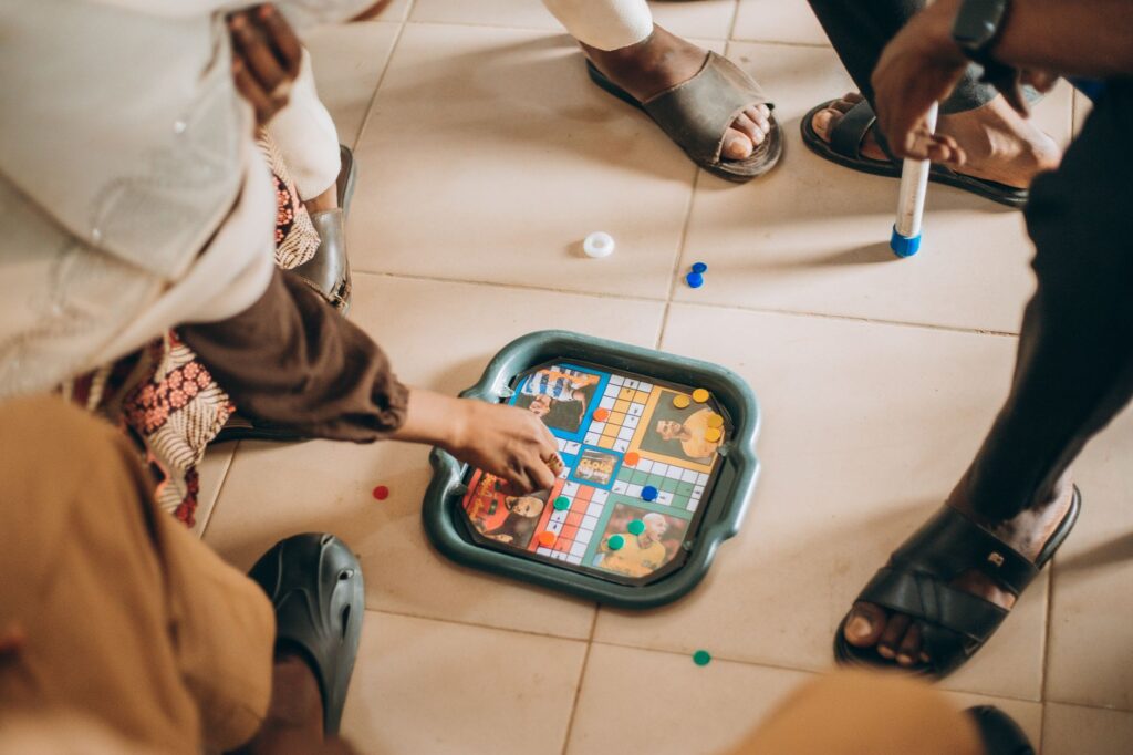 Group of children playing board game indoors on a tiled floor, focused on the game pieces.