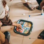 Group of children playing board game indoors on a tiled floor, focused on the game pieces.