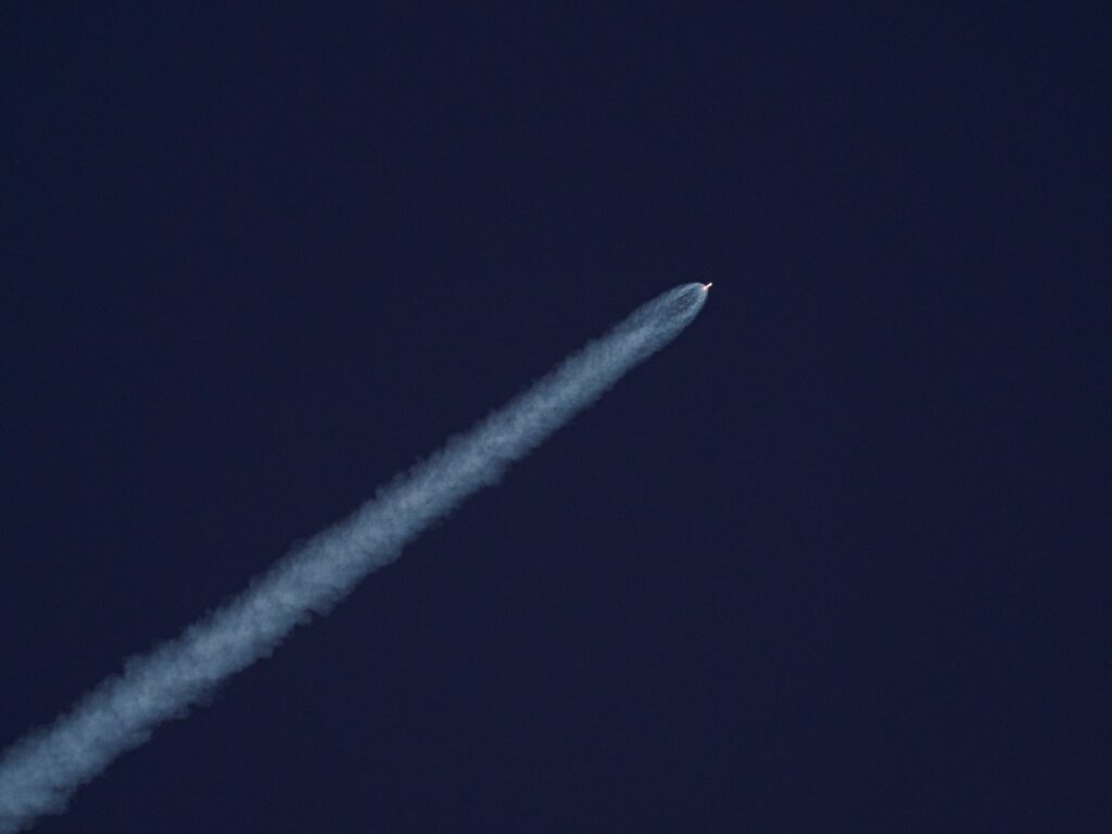 A rocket ascends into the sky, leaving a trail of smoke against the clear blue sky.