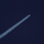 A rocket ascends into the sky, leaving a trail of smoke against the clear blue sky.