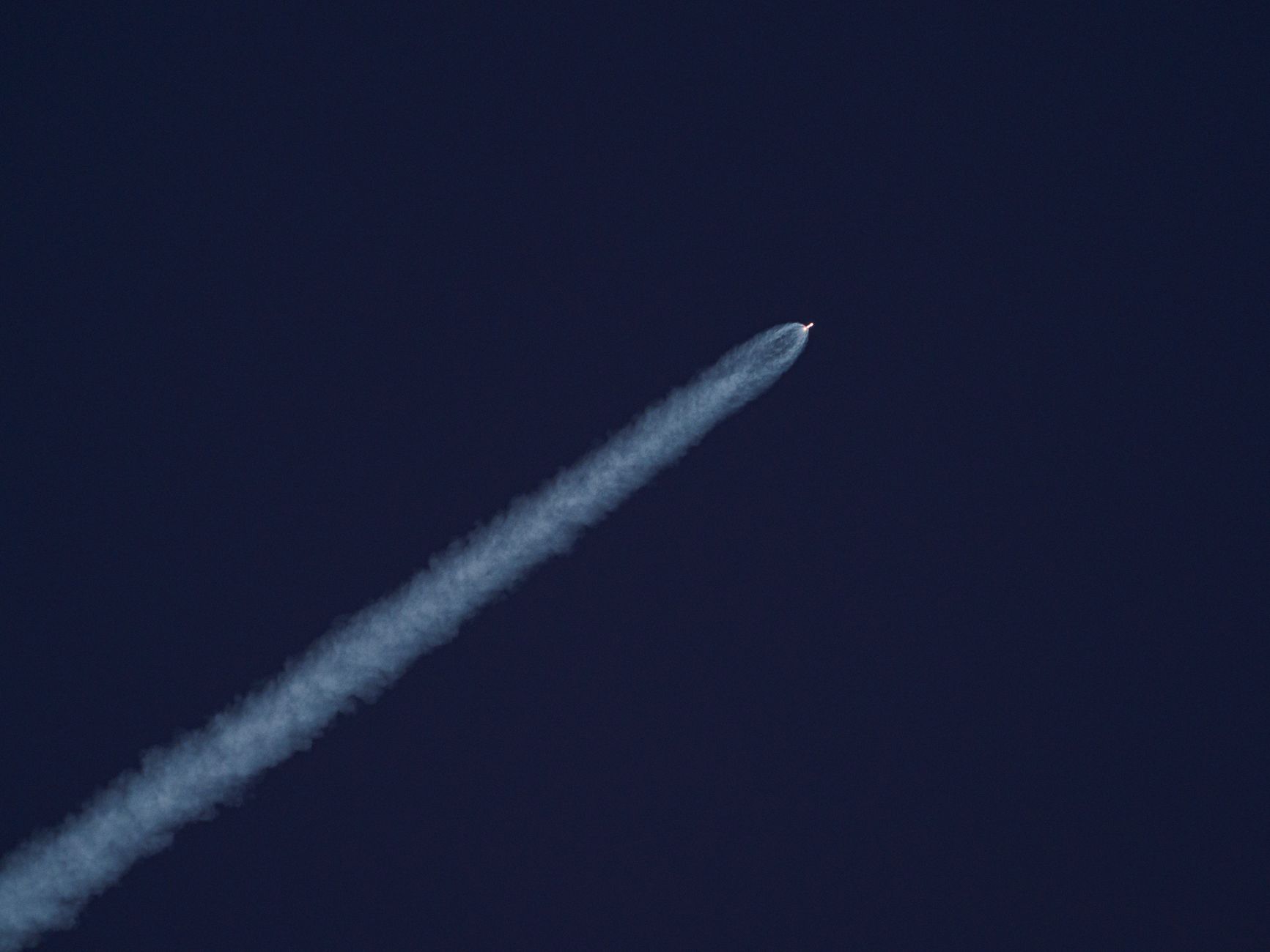 A rocket ascends into the sky, leaving a trail of smoke against the clear blue sky.