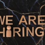 Wooden letters spell 'We Are Hiring' on dark marble surface.