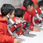 Young students in red exploring science with microscopes in a classroom setting.