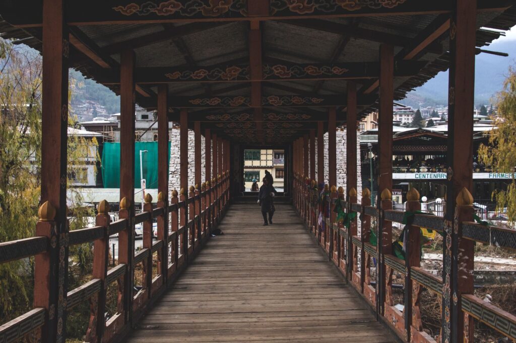 A person walks across a narrow, traditional wooden bridge in Thimphu, Bhutan, showcasing local architecture.