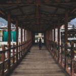 A person walks across a narrow, traditional wooden bridge in Thimphu, Bhutan, showcasing local architecture.