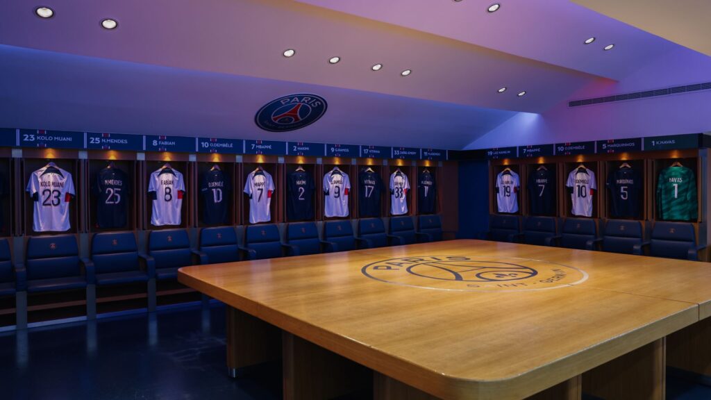 Interior view of Paris Saint-Germain's locker room featuring team jerseys and emblem.