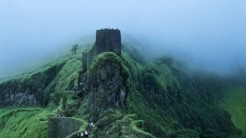 Lush greenery surrounds the historic Sinhagad Fort in Pune, India, enveloped in monsoon mist.
