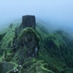 Lush greenery surrounds the historic Sinhagad Fort in Pune, India, enveloped in monsoon mist.
