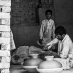 A father and son crafting traditional pottery inside a clay-brick building.