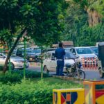 A policeman manages heavy traffic on a bustling street in Lahore, Pakistan, amidst greenery and urban chaos.